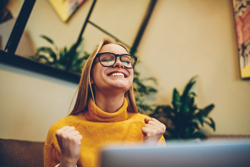 Mulher em frente ao notebook comemora a experiência de usuário na sua navegação no site.