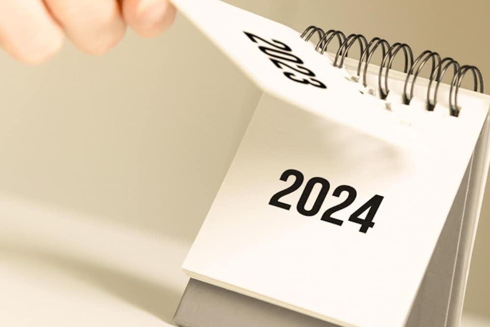 Pessoa virando a página de um calendário de 2023 para 2024.