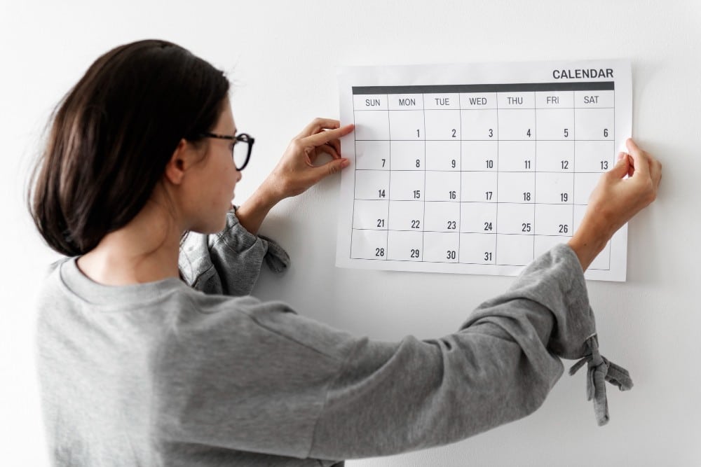 Mulher pendurando na parede um calendário do ano de 2024.
