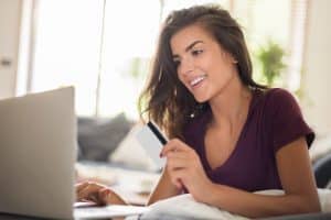 mulher sentada com um notebook na mesa enquanto segura um cartão de crédito e olha para tela do notebook