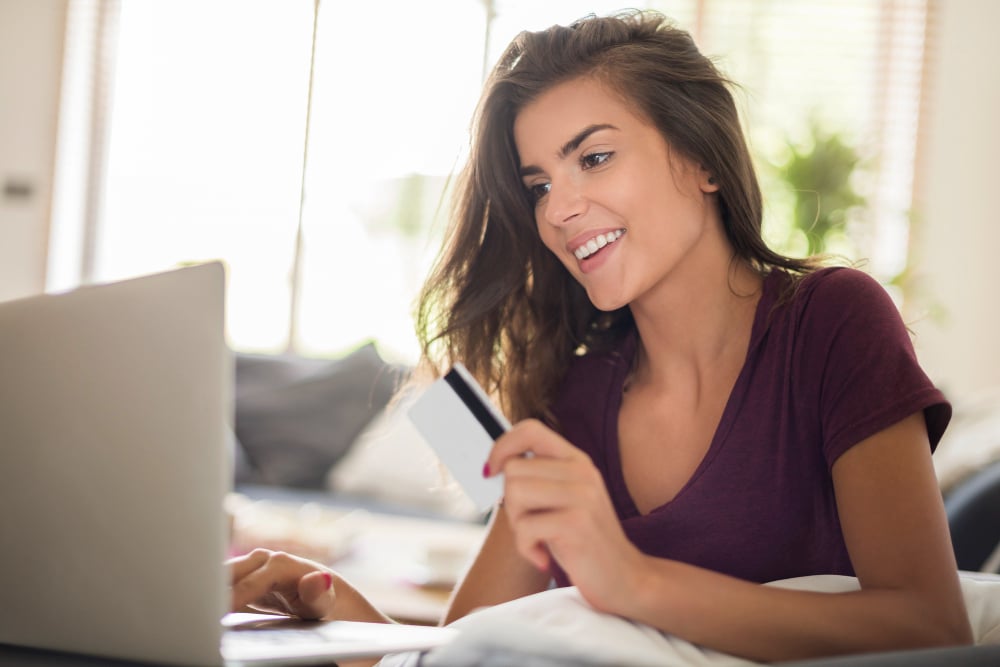 mulher sentada com um notebook na mesa enquanto segura um cartão de crédito e olha para tela do notebook