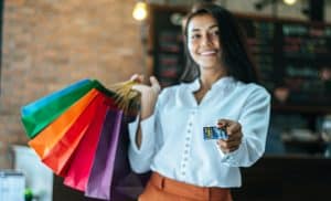 mulher-com-blusa-branca-com-um-cartao-em-uma-das-mao-e-na-outra-sacolas-de-compras.