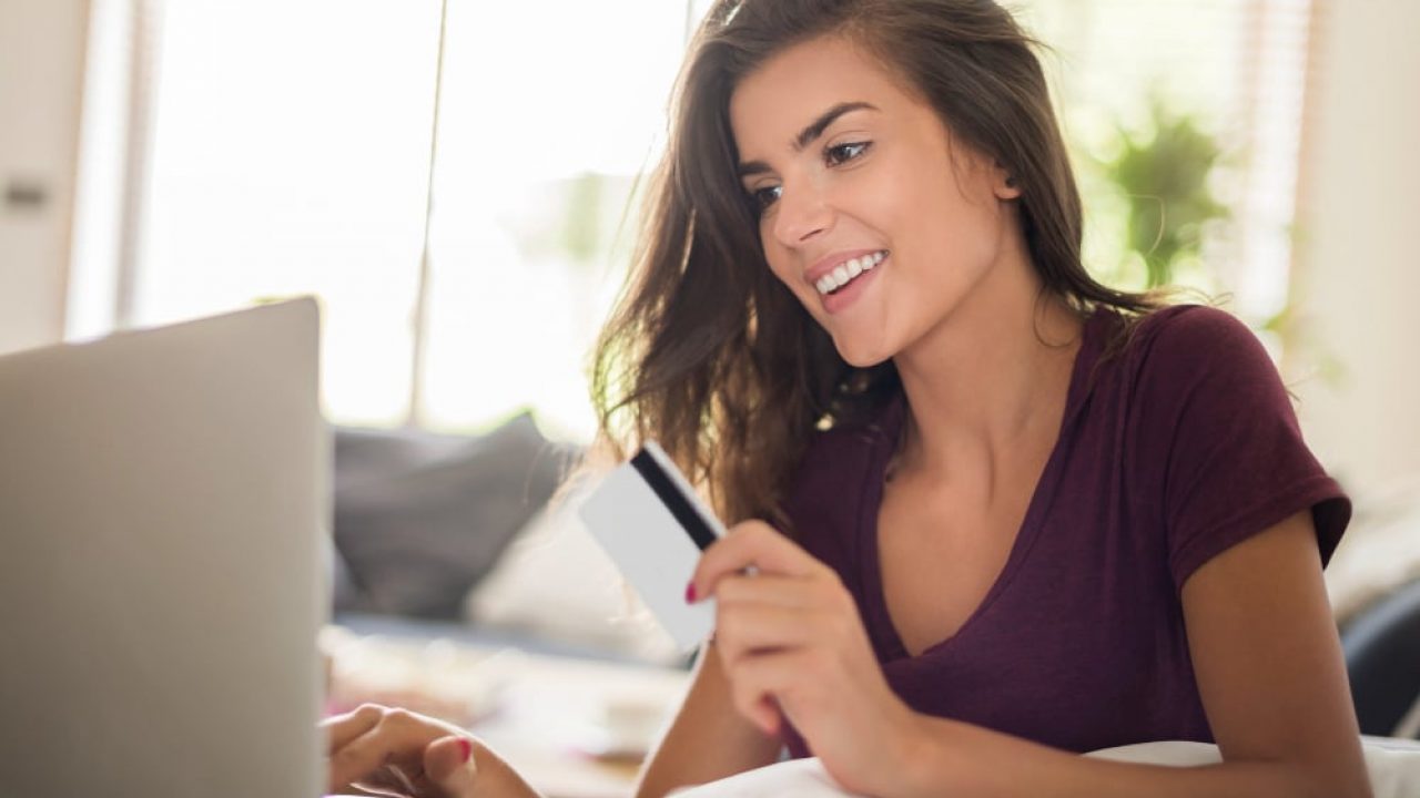 mulher sentada com um notebook na mesa enquanto segura um cartão de crédito e olha para tela do notebook