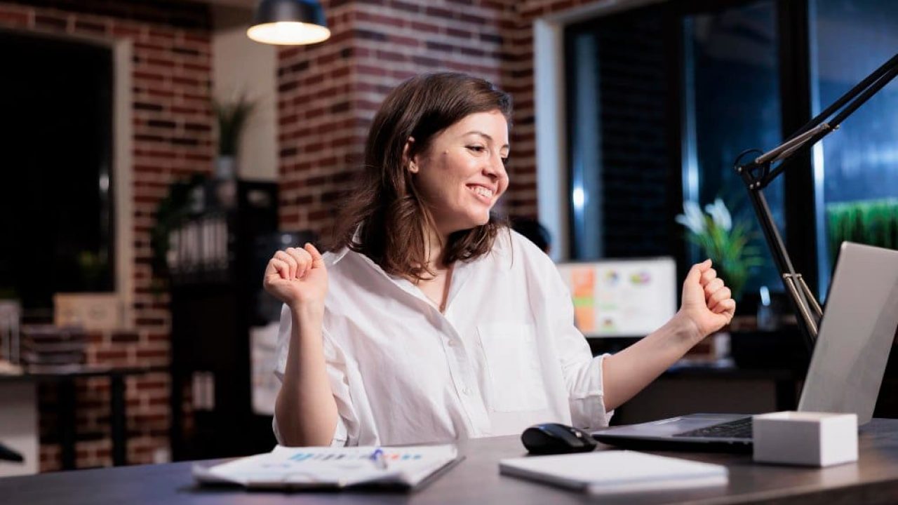 Mulher comemorando enquanto olha para a tela do computador.